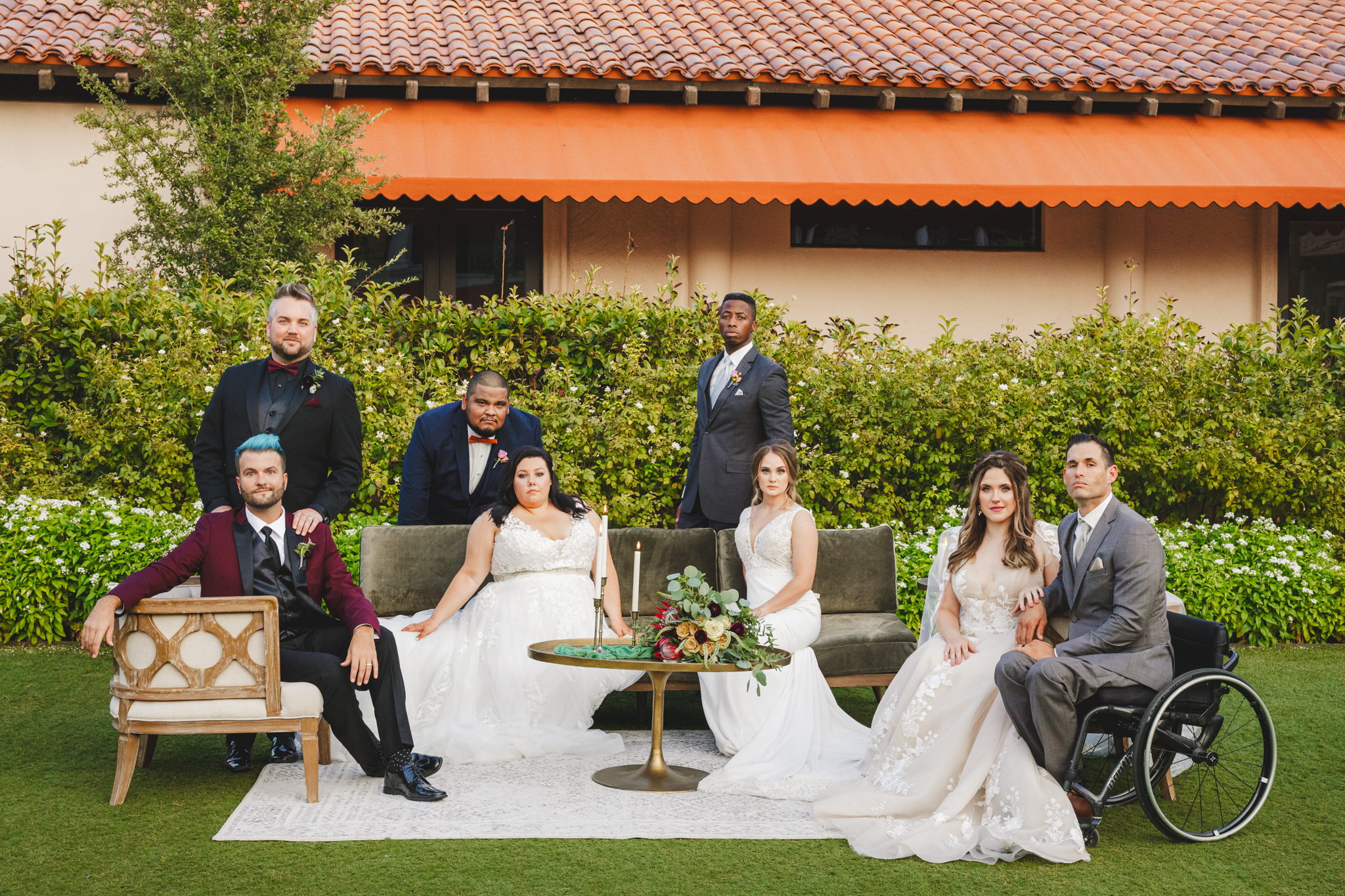 A diverse group of brides and grooms poses in front of furniture at a resort
